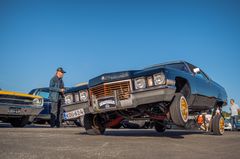 Mies seisoo mustan lowrider-auton vieressä, jonka keula on kohotettuna ylös.