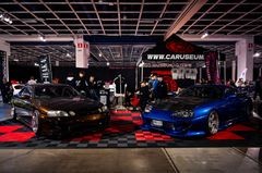 Kaksi autoa ja ihmisiä autotapahtumassa näyttelyhallissa.