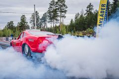 Punainen auto savuverhossa kilparadalla metsäisellä alueella kesällä.