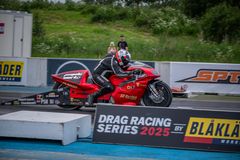 Moottoripyöräilijä kiihdyttelee radalla drag racing -kilpailussa. Taustalla mainoksia.