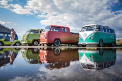 Soraparkkialueella on kolme värikästä klassikkoautoa, jotka peilautuvat lätäköstä.