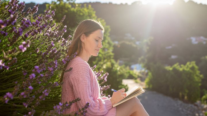 paikan-poetiikka-kirjoittamiskurssi-Lohja-Hiiden-Opisto-nainen-kirjoittaa-luonnossa-aurinko-paistaa