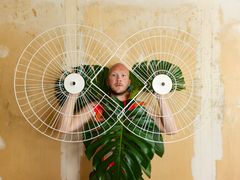 Alt-text: Henkilö pitelee kahta suurta metallista kehikkoa ja suuria lehtiä kasvojensa edessä.