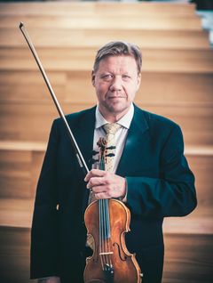 Lohjan kaupunginorkesterin konserttimestari Tero Latvala juhlapuvussa seisoo portaikossa pitäen viulua ja jousia kädessään.