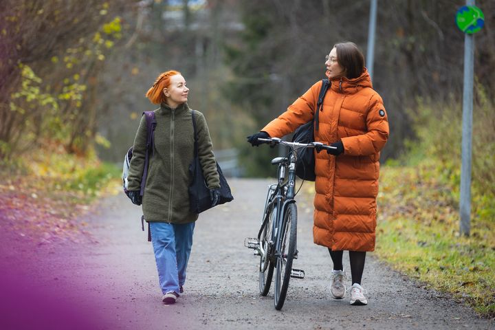 Kaksi naista kävelevät syksyisellä kadulla ja katsovat toisiinsa.