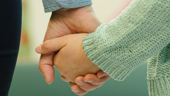 Lapsi ja aikuinen pitelevät toisiaan kädestä.