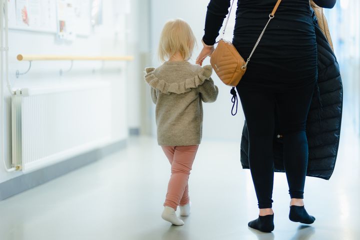 Pieni lapsi ja aikuinen kävelevät käytävällä, lapsi pitää aikuisen kädestä kiinni.