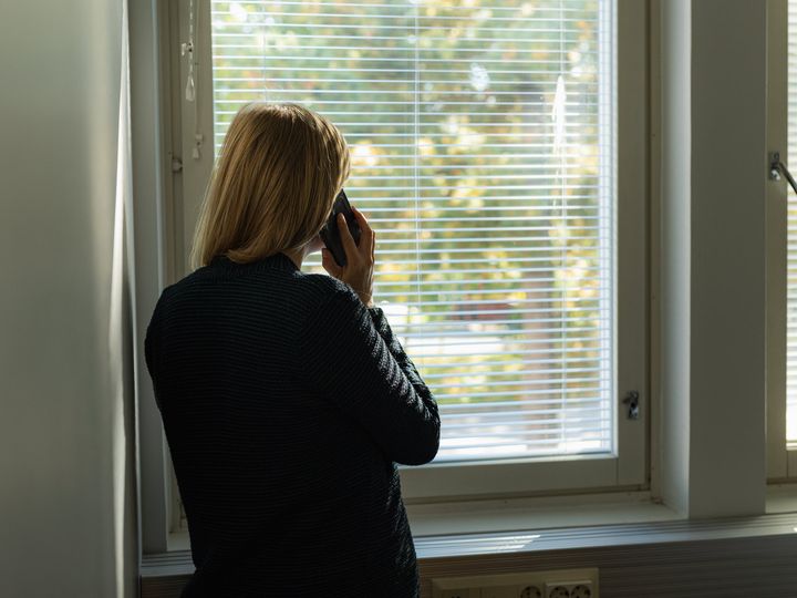 Henkilö seisoo ikkunan edessä puhelimessa.