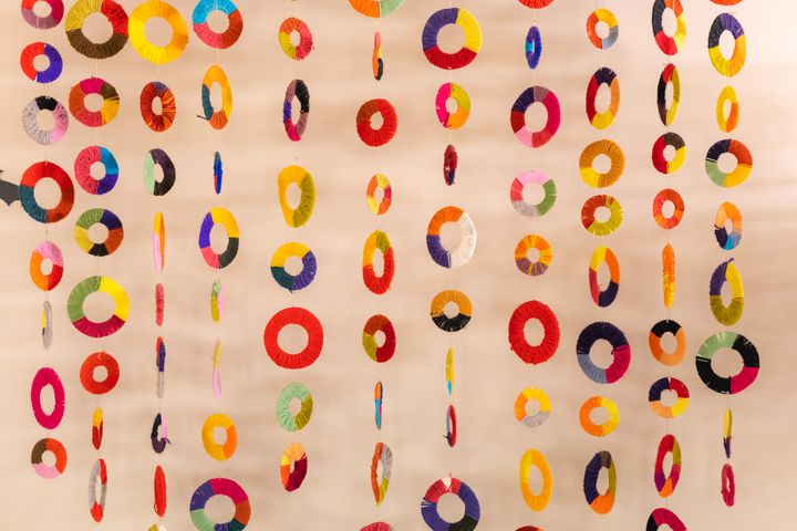 Värikkäitä pyöreitä koristeita roikkuu riveissä vaalealla taustalla.