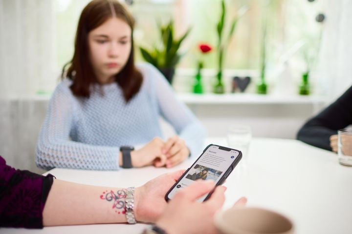 Henkilö käyttää älypuhelinta kahvilassa muiden seurassa.