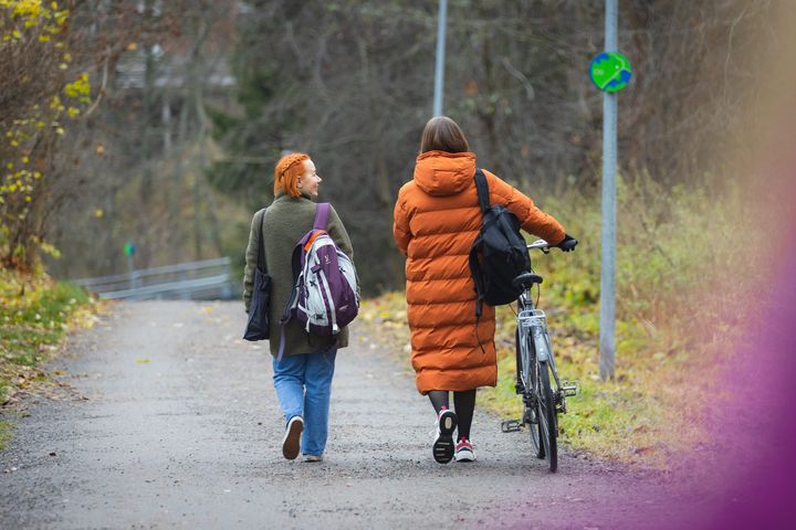 Kaksi henkilöä kävelee syksyisellä polulla, toinen työntää polkupyörää.