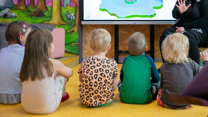 Lapset päiväkodissa istumassa lattialla ja kuuntelemassa tarinaa.