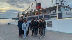 Kahdeksan henkilöä seisoo laiturilla laivan edessä.