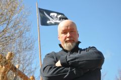 Tuomas Kuhmonen lähikuvassa ulkona, taustalla merirosvolippu.