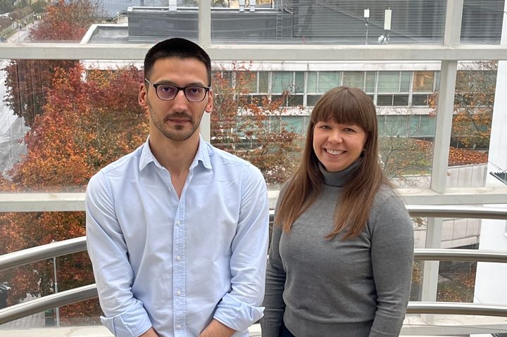 Kaksi henkilöä poseeraa sisätiloissa ikkunan edessä.