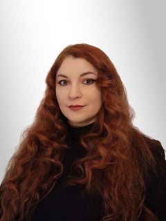 Väittelijän potrettikuva, nainen katsoo kohti kameraa, naisella on pitkät punaiset kiharat hiukset ja yllään musta poolokauluksinen pusero