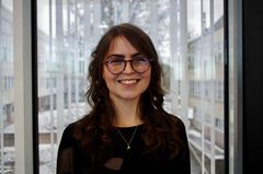 Väittelijän profiilikuva, tummahiuksinen ja silmälasipäinen nainen mustassa puserossa hymyilee ja katsoo kohti kameraa