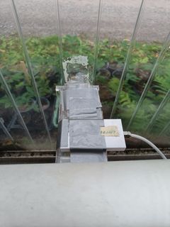 Kasvihuoneen seinän läpi menevä putki, johon on kiinnitetty lukija.