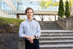 Turun yliopiston kampuksella kesäisenä päivänä otettu ulkokuva. Lauri Karttunen seisoo rakennuksen vieressä olevassa ulkoportaikossa ja katsoo kohti kameraa. Takana näkyy portaikkoa, rakennuksen seinää ja rakennusten välinen nivel