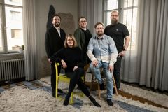 En grupp av fem personer poserar tillsammans i ett rum. Fyra står, och en sitter på en stol.