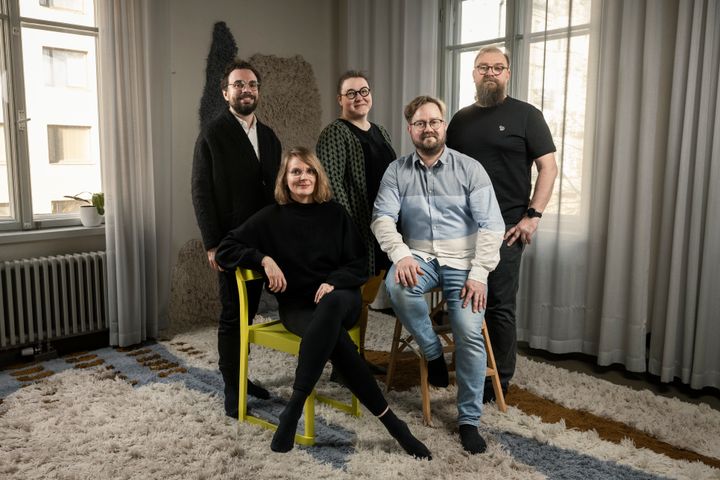 Viisi henkilöä poseeraamassa ryhmäkuvassa valoisassa huoneessa.