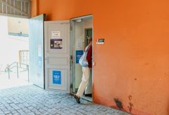Henkilö astuu sisään oranssiseinäiseen rakennukseen avonaisesta ovesta.