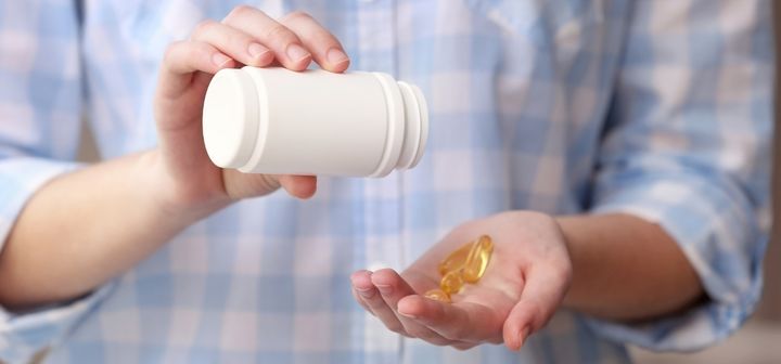 Henkilö pitää valkoista pilleripurkkia ja kaataa ravintolisäkapseleita kädelleen.