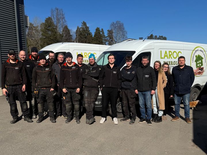Laroc-henkilökunnan ryhmäkuva ulkona, taustalla kaksi pakettiautoa.