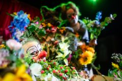 Kuvassa kaksi klovnia. Toinen hautautuu kukkamereen ja toinen lymyilee suden kanssa taustalla.