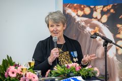 Kyra Kyrklund pitää puhetta mikrofonilla, rinnassa ansiomerkki, pöydällä kukkia.