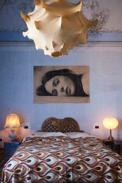 Makuuhuone Palazzo Cirillossa, jossa sängyssä koristeellinen vuodepeite, kaksi lamppua yöpöydillä sekä suuri katseenvangitseva kattovalaisin.