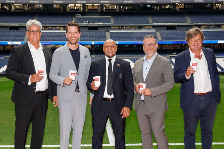 Five men standing on a soccer field holding cards, smiling at the camera. From left: Patrick Schenk (responsible for sports partnerships at the Melitta Group), Jero Bentz (member of the management board and great-grandson of company founder Melitta Bentz), Roberto Carlos (soccer legend and youth coach at Real Madrid), Roberto Rojas Martin (responsible for human resources at the Melitta Group), Leonardo Herran López de Montenegro (country manager Melitta Spain).