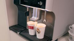 A Melitta XT6 coffee machine dispensing coffee into cups with logos at Bernabeu Stadium.