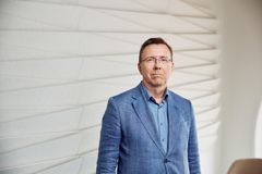 Jouni Salmenkivi sinisessä puvussa seisoo nykyaikaisen seinän edessä.
