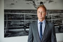 Harri Kojonen pukeutuneena pukuun seisoo taideteoksen edessä, jossa on kuva merimaisemasta.