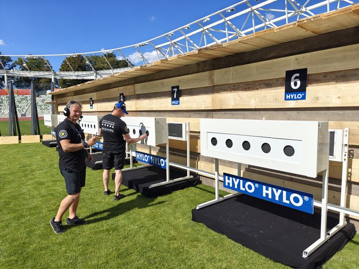Uutta ampumataulujärjestelmää testattiin elokuussa Dresden City Biathlon -tapahtumassa Saksassa. Lyijynkeräin erottuu ampumataulujen takana. Kuvassa Suomen Biathlon Oy:n teknikot tarkastamassa paikalle asennettuja läpiammuttavia ESB-2 -ampumatauluja.