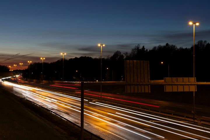 Moottoritie iltahämärässä, katuvalot valaisevat tietä ja autojen valot piirtävät pitkiä juovia.