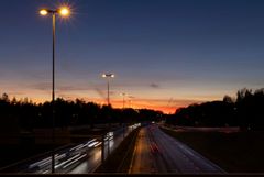 Moottoritie iltahämärässä katuvalojen valaisemana, taustalla auringonlasku.