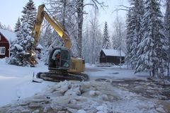 Kaivinkone työskentelee jäätyneellä joella talvisessa maisemassa.