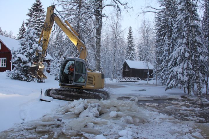 Kaivinkone työskentelee jäätyneellä joella talvisessa maisemassa.