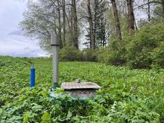 Pieni pumppaamo nurmikolla metsäisellä alueella, jossa taustalla puita.