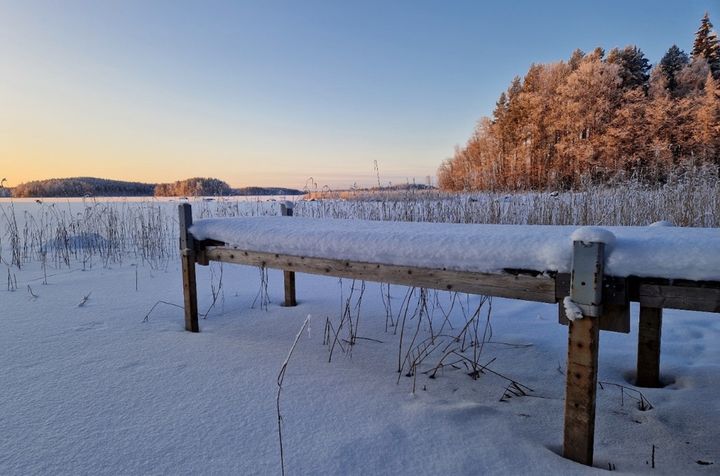 Talvinen Saimaa järvimaisema Savonlinnassa, aurinko laskee lumisen maiseman yllä, kuuraisia puita taustalla.