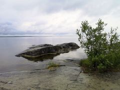 Kuvassa merellinen maisema rannalta päin. Etualalla kalliota ja pusikkoa.