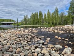 Vuolas joki jossa on runsaasti kiviä, taustalla silta ja vehreää metsää.