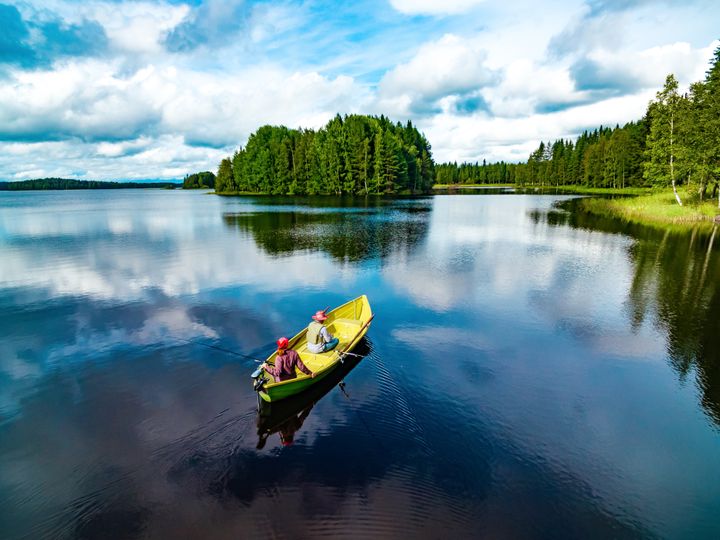 Två personer som fiskar från en båt mitt i ett finskt sjölandskap.