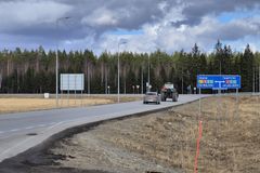 Auto ja traktori ajavat maantiellä, tienviitat näyttävät suuntia kohti Vaasaa, Seinäjokea ja Tamperetta, taustalla metsää.
