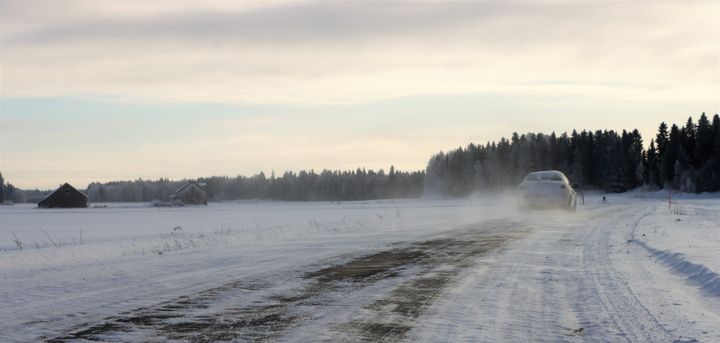 Auto ajaa talvisella, vähälumisella tiellä maaseudulla.