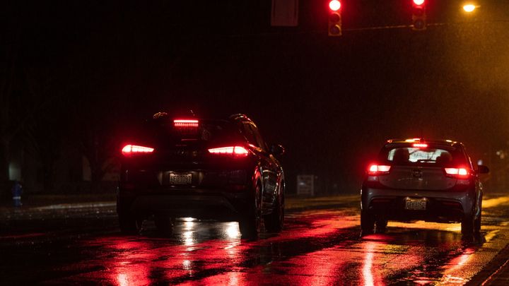 Kaksi autoa odottaa liikennevalojen muuttumista pimeällä tiellä.