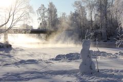 Talvinen maisema Pielisjoelta Joensuussa, pakkaslumi peittää maan ja sumua nousee vedenpinnalta sillan edustalla. Etualalla pieni lumiukko.