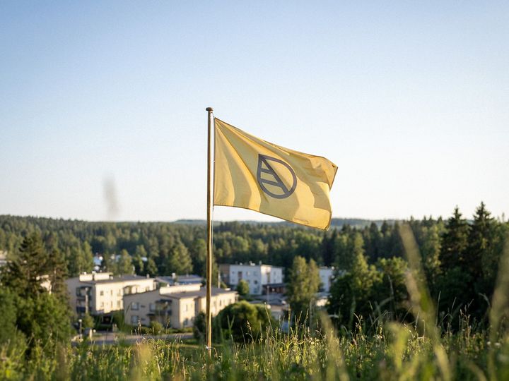 Keltainen lehtilippu liehuu sangossa ja taustalla metsää ja puita.